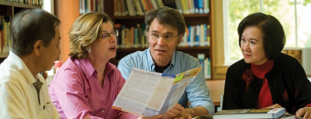 Four people sitting at a table in the library, looking at and discussing a brochure